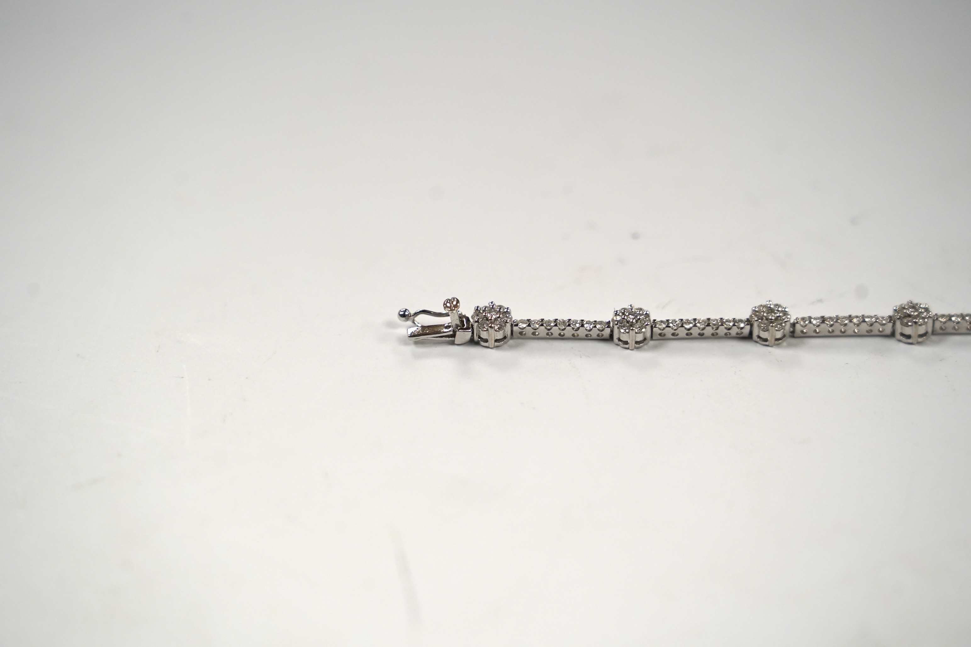 A modern 18k white metal and diamond cluster set line bracelet, 17.8cm, gross weight 8.8 grams.